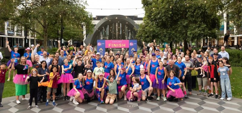 Runners and supporters in pink tutus and blue singlets under the Mountain to Melbourne finish arch at Eastland Town Square, 2025